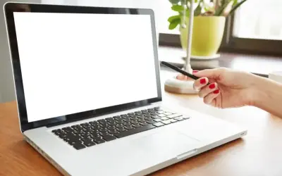 Dłoń z czerwonymi paznokciami wskazuje na biały ekran laptopa.