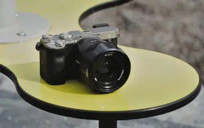 Srebrno-czarny aparat Sony a7c z obiektywem na żółtym stoliku.