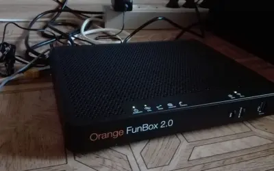 Czarny router Orange FunBox 2.0 z wieloma kablami podłączonymi do listwy zasilającej.