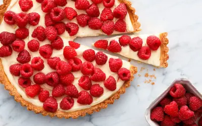 Pyszna tarta z malinami, udekorowana kremem i świeżymi malinami. Jeden kawałek już został wyjęty.