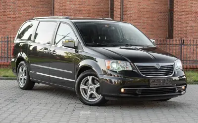 Czarny Lancia Voyager stoi na brukowanym podjeździe przed ceglanym budynkiem.