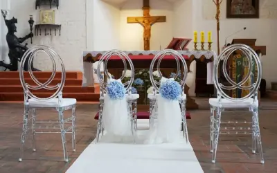 Elegancka dekoracja kościoła na ślub samemu: przezroczyste krzesła z błękitnymi kwiatami i tiulem, biały dywan prowadzący do ołtarza.