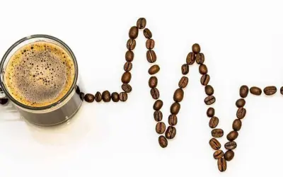 Tazza di caffè con chicchi disposti a formare un elettrocardiogramma, simbolo della caffeina nel caffè che stimola il cuore.
