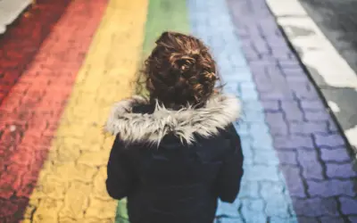 Dziecko z kręconymi włosami idzie po tęczowym przejściu dla pieszych.