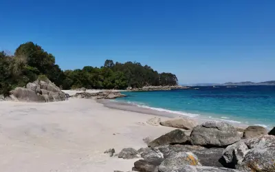 Arena blanca, aguas turquesas y rocas salpican la **playa de Castiñeiras**, un rincón idílico bajo un cielo azul intenso.