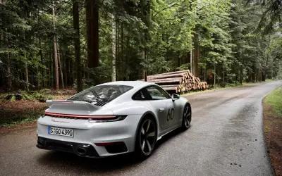 Ein weißer Porsche 911 mit der Nummer 60 auf der Seite fährt auf einer nassen Waldstraße. Die Beschleunigung von 0 auf 100 km/h ist beeindruckend.