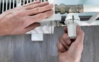 Mano ajusta el termostato de un radiador. El radiador solo calienta la mitad derecha, indicando un posible problema.