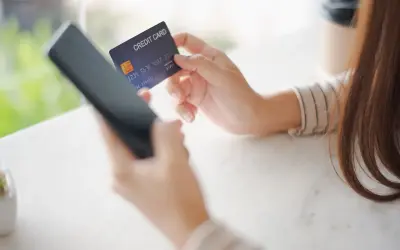 Kobieta trzyma kartę kredytową i telefon, przygotowując się do płatności online. W razie problemów z transakcją, może skorzystać z procedury chargeback.