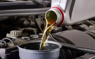 Huile moteur versée dans un entonnoir, étape clé avant la vidange par aspiration. Le moteur de la voiture est visible en arrière-plan.
