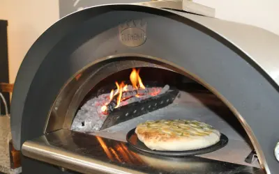Una crescia dorata pronta per essere infornata in un forno a legna Clementi, con fiamme vive che creano l'atmosfera perfetta per la ricetta.