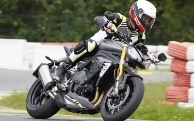 Motocyklista w kasku i kombinezonie pochyla się na torze wyścigowym na motocyklu Triumph Speed Triple.