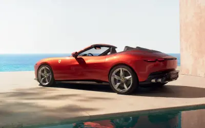 Czerwony Ferrari Spider z otwartym dachem, zaparkowany przy basenie z widokiem na morze.