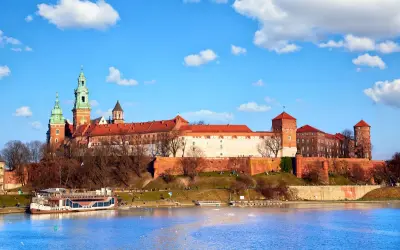Majestatyczny Wawel góruje nad Wisłą. Widok na wejście na Wawel z rzeki, z widoczną barką i błękitnym niebem.