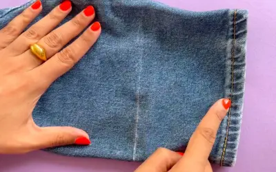 Main d'une femme avec un ongle rouge vif et une bague dorée, ajustant l'ourlet d'un jean.