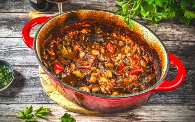 Herzhaftes Kalbsgulasch im roten Bräter, ein köstliches Rezept mit Paprika und Zwiebeln, bereit zum Servieren.