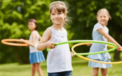 Uśmiechnięte dziewczynki biorą udział w konkurencjach sportowych dla dzieci, kręcąc hula-hop na trawie.