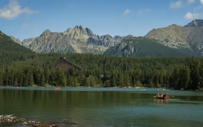 Malownicze jezioro na Słowacji blisko granicy, otoczone lasem i górami. Na wodzie widać łodzie, a w tle hotel w kształcie trójkąta.
