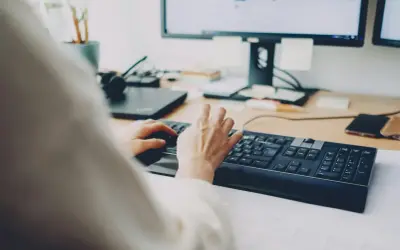 Dłonie piszą na klawiaturze, za nimi monitor. Szybkie załatwienie sprawy, może zwolnienie lekarskie online?