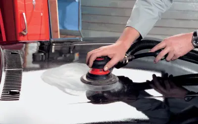 Mani esperte utilizzano una levigatrice per stuccare auto, preparando la carrozzeria per una finitura impeccabile.