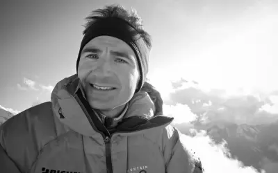 Ueli Steck, lächelnd in warmer Bergkleidung, blickt in die sonnige, wolkenverhangene Bergwelt.