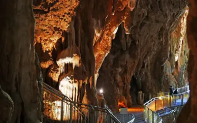 Sentiero illuminato tra le stalattiti delle grotte di Pastena, con persone che passeggiano.