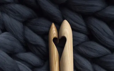Dwa drewniane szydełka tworzą serce na tle grubiutkiej, ciemnoszarej wełny merino. Co to jest wełna merino? To miękkie włókno idealne do dziergania.