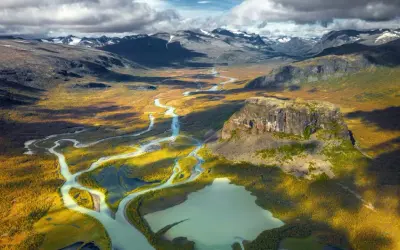 Weites Tal mit Fluss und Berg in Schwedens Nationalparks. Herbstliche Farben und dramatische Wolken über der Landschaft.