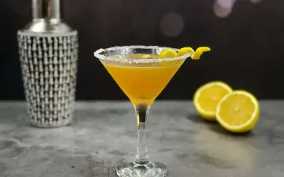 Elegancki koktajl Sidecar w kieliszku z cukrowym rantem, obok cytryny i shakera.