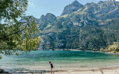 Chłopiec bawi się na plaży nad Jeziorem Garda, w tle góry. Idealne pola kempingowe czekają na odkrycie.