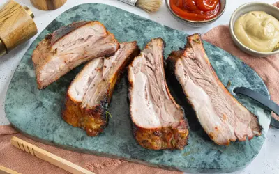 Saftige, dicke Rippe vom Grill, perfekt gegart und auf einem grünen Marmorbrett angerichtet. Dazu passen Ketchup und Senf.