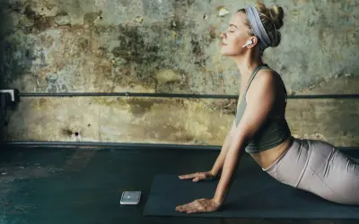 Mujer en postura de cobra, con auriculares, meditando. Considera las contraindicaciones de la postura de la cobra si tienes problemas de espalda.
