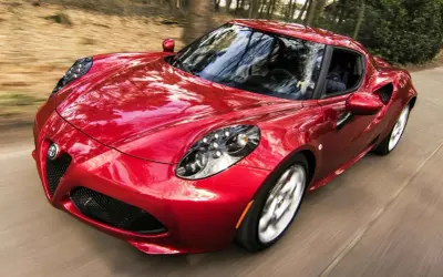 Czerwone Alfa Romeo 4C z połyskiem lakieru perłowy a metalik, pędzące przez las.