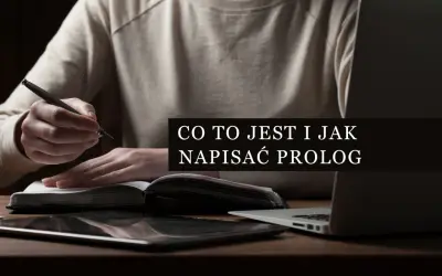 Osoba pisze piórem w notatniku, obok leży tablet i laptop. Tekst na ekranie: "Co to jest i jak napisać prolog".