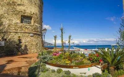 Laigueglia centro storico: torre medievale, barca fiorita e mare blu.