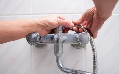 Hands working to fix a shower faucet, detaching the shower hose.