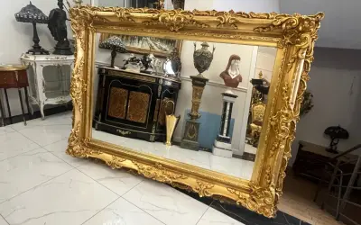 Wspaniałe lustro w bogatej, złotej ramie, odbijające antyczne meble i dekoracje.