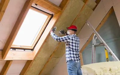 Mann isoliert ausgebauten Dachboden mit Dämmmaterial. Ein Dachfenster sorgt für Licht.