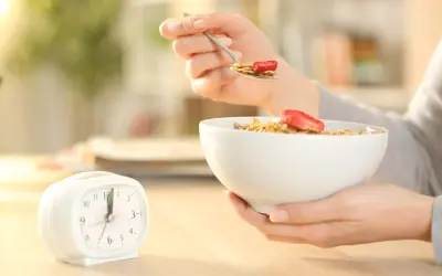 Une personne mange des céréales avec des fraises, une horloge à côté. Le jeûne intermittent avant après 1 mois, une nouvelle habitude alimentaire.