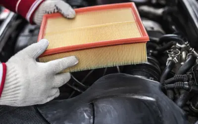 Mains gantées tenant un filtre à air propre, prêt à remplacer un filtre à air encrassé dans un moteur de voiture.