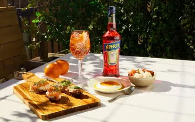 En Aperol Spritz med tilltugg till aperol spritz: laxsnittar, ost med honung och inlagda grönsaker.
