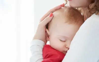 Ciemiączko przednie niemowlęcia delikatnie dotykane przez matkę. Dziecko śpi wtulone w jej ramię.