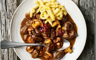 Herzhaftes Rehgulasch mit Rotwein, Pilzen und Preiselbeeren, serviert mit Spätzle. Ein köstliches rehgulasch rezept mit rotwein.