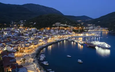 Widok na oświetlone miasto Parga nad morzem o zmierzchu, z górami w tle.