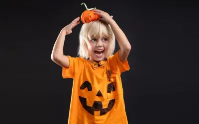 Chłopiec w pomarańczowej koszulce z namalowaną buźką dyni i mini dynią na głowie. Idealny pomysł, jak zrobić strój dyni z bibuły na Halloween!