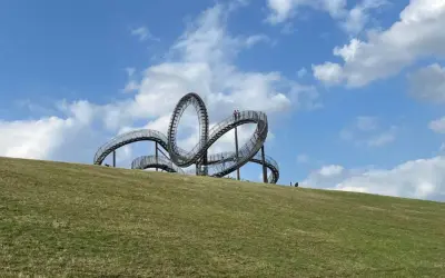 Ein skulpturales Kunstwerk auf einem Hügel, das an eine Achterbahn erinnert. Perfekt für spannende Ausflugsziele mit Kindern.