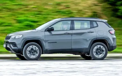 Szary Jeep Compass 4xe w ruchu, z rozmytym zielonym tłem.