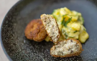 Zwei goldbraune Fischbuletten, eine aufgeschnitten, daneben Kartoffelsalat. Ein leckeres Fischbuletten Rezept.