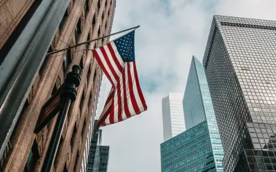 Amerykańska flaga powiewa między drapaczami chmur. Zastanawiasz się, ile kosztuje ubezpieczenie w USA?