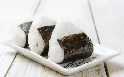 Trzy pyszne onigiri, czyli japońskie kulki ryżowe zawinięte w nori, leżą na białym talerzyku.