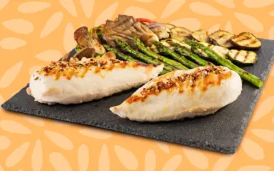 Dos jugosas pechugas de pollo a la parrilla, sazonadas con especias, acompañadas de espárragos, calabacín y champiñones.
